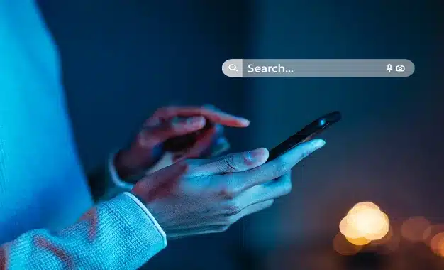 A person holding a mobile phone in hand and a search box appearing above his hand